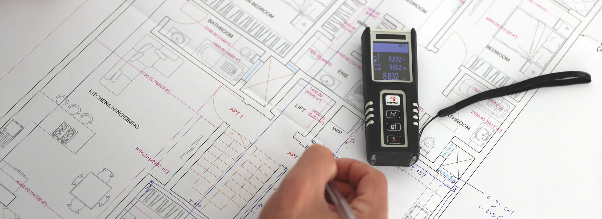 Hand mit Stift über einem technischen Bauplan mit Messgerät darauf